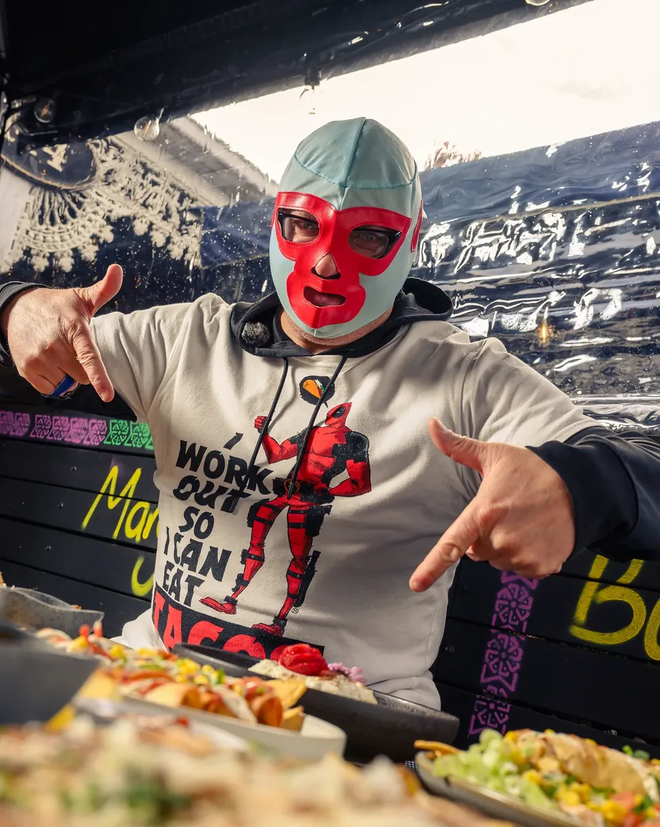 Luchador offering a taco in front of the mural